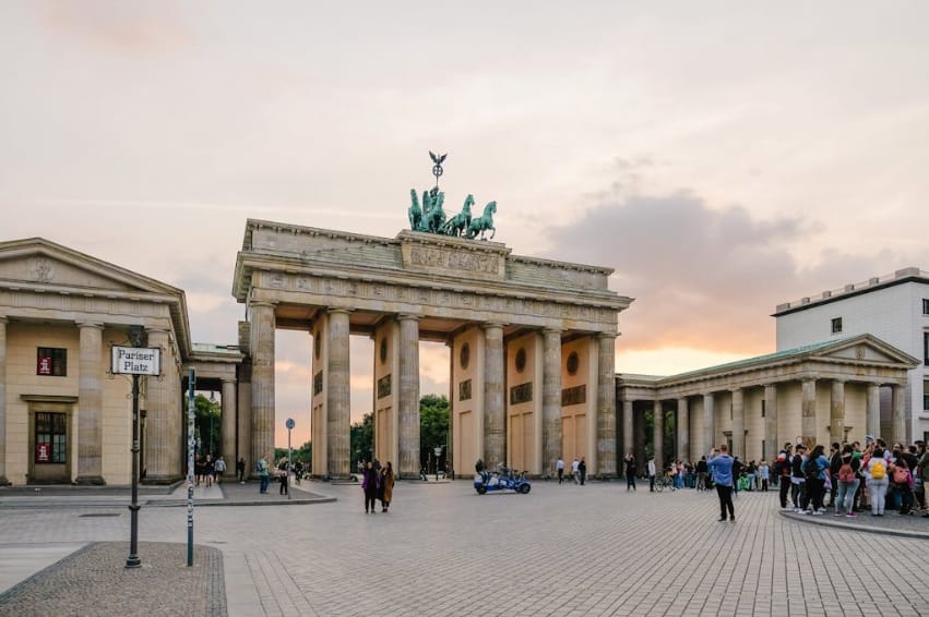 Scenic view of Berlin's Brandenburg Gate with people gathering at sunset.