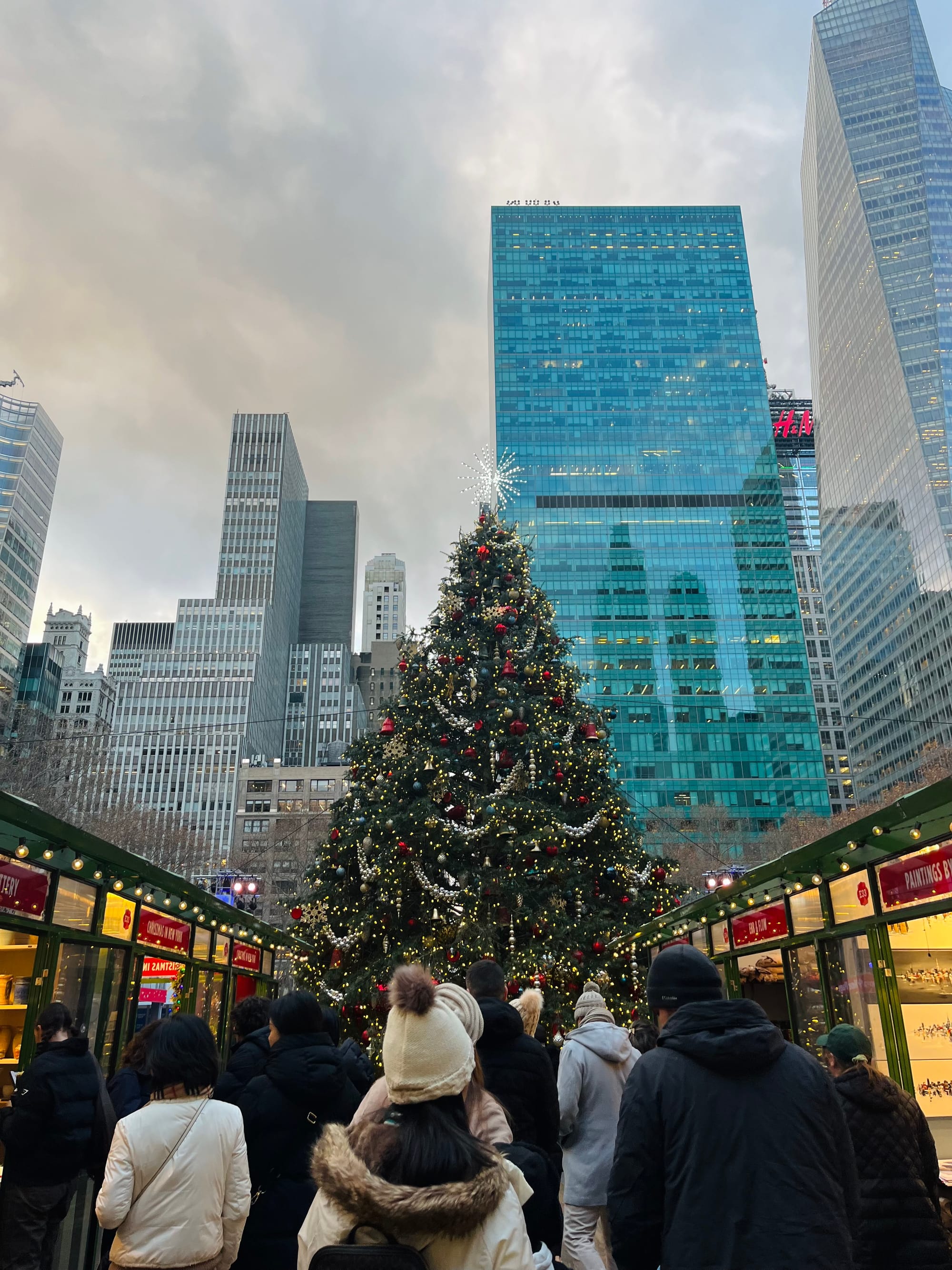 A tall Christmas tree in the centre, a crowd of people walking toward it.