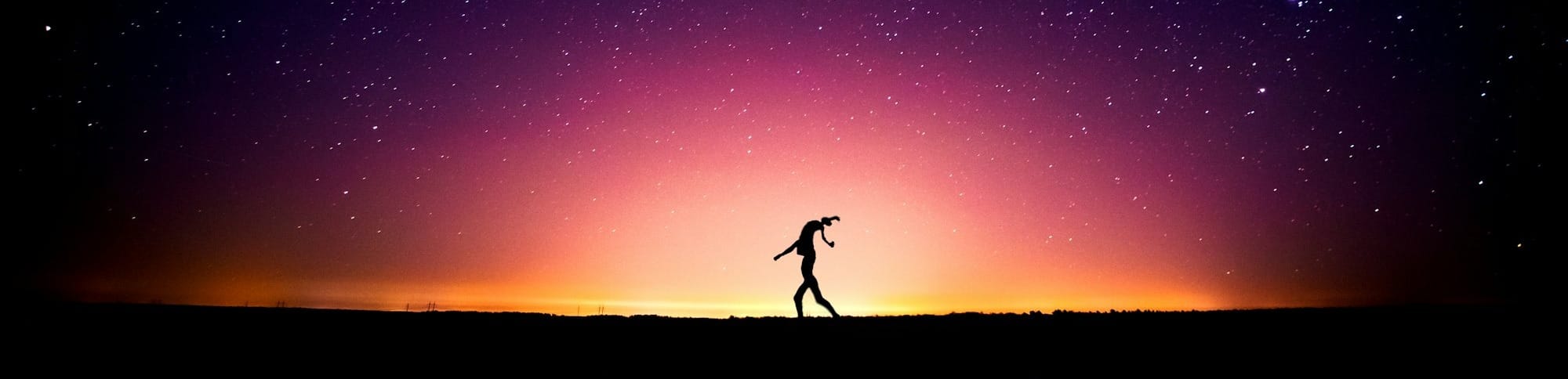 silhouette of person standing on rock under starry night