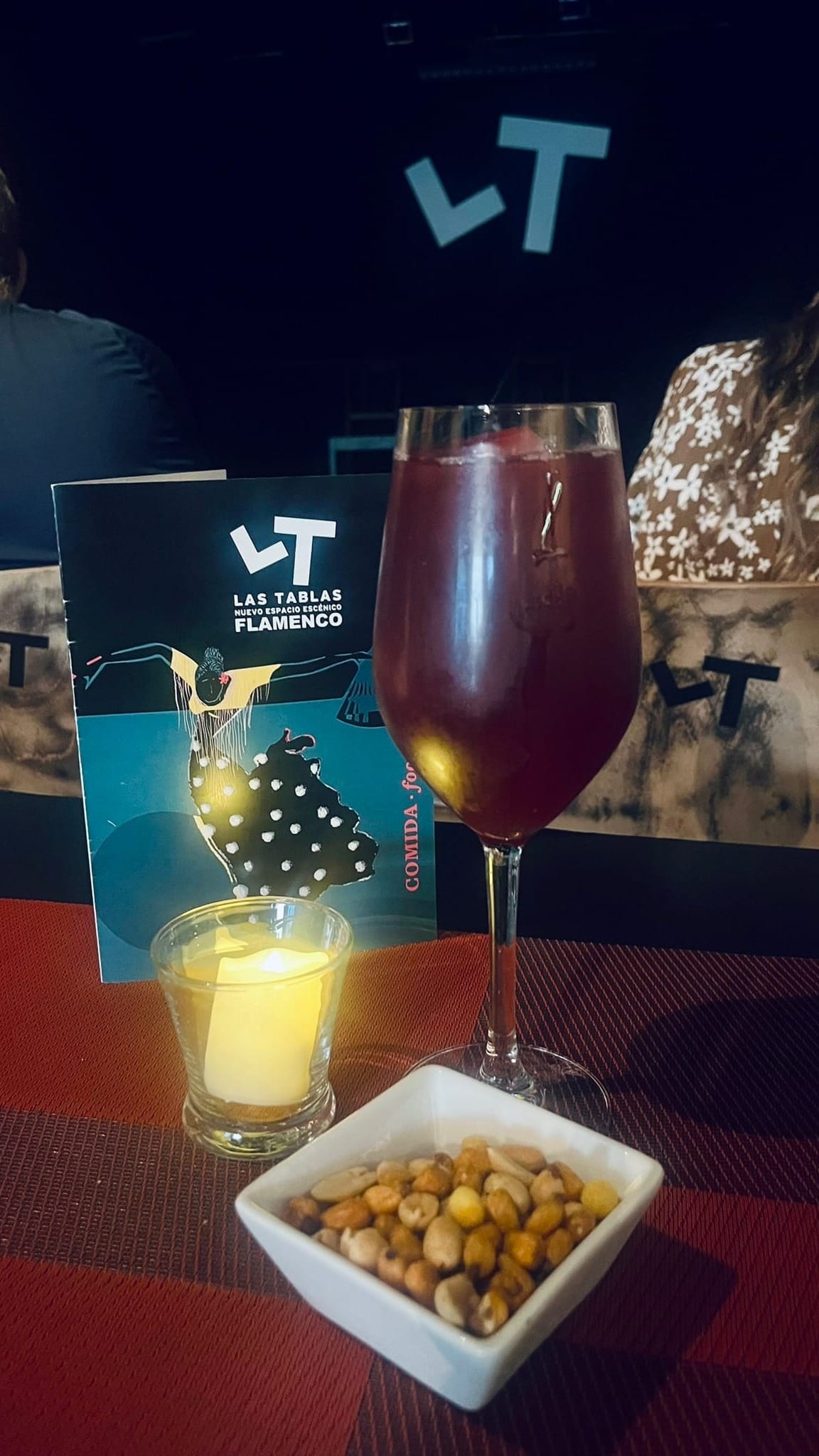 glass of wine, bowl of nuts, candle, and programme