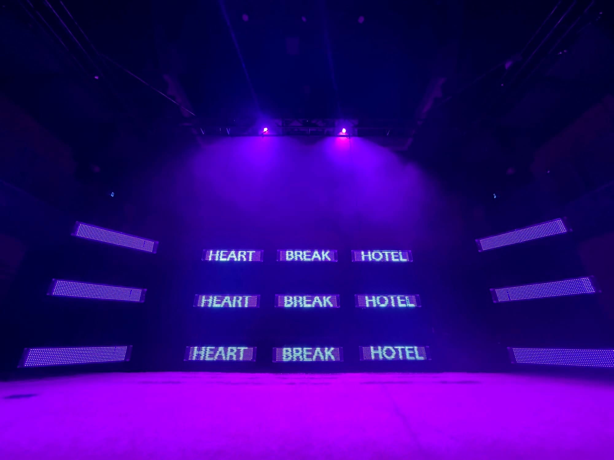 stage shining purple and blue light with LEDs spelling out "heart break hotel" 