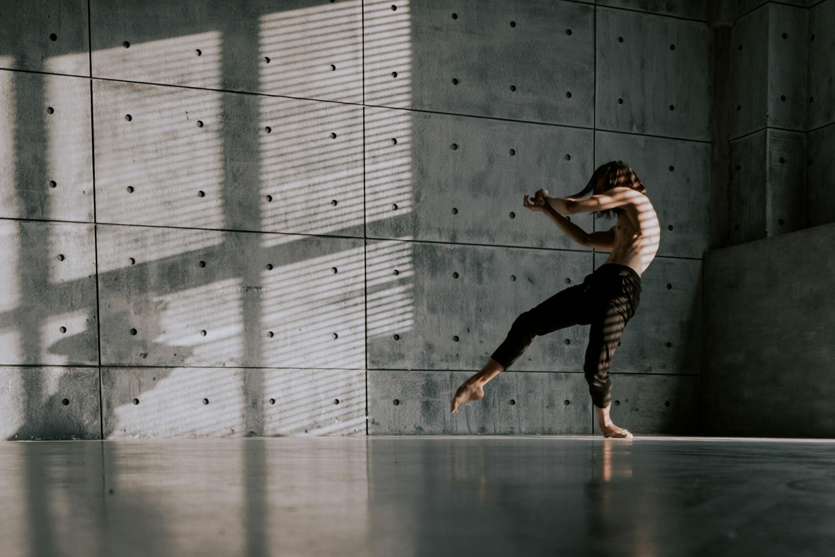 A male dancer performs a contemporary routine in a minimalist dance studio, capturing motion and expression.